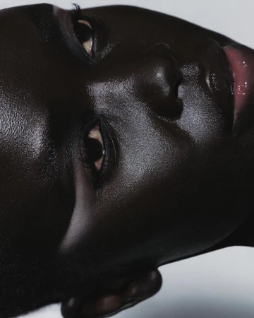 Close-up portrait of a dark-skinned model with glossy skin and detailed eye makeup captured by Antoine And Charlie in Paris.