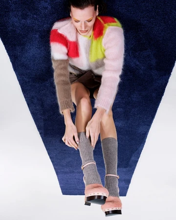 Overhead shot of a stylish woman with a multicolored sweater, mini skirt, socks, and platform heels, posing on a blue and white carpet.