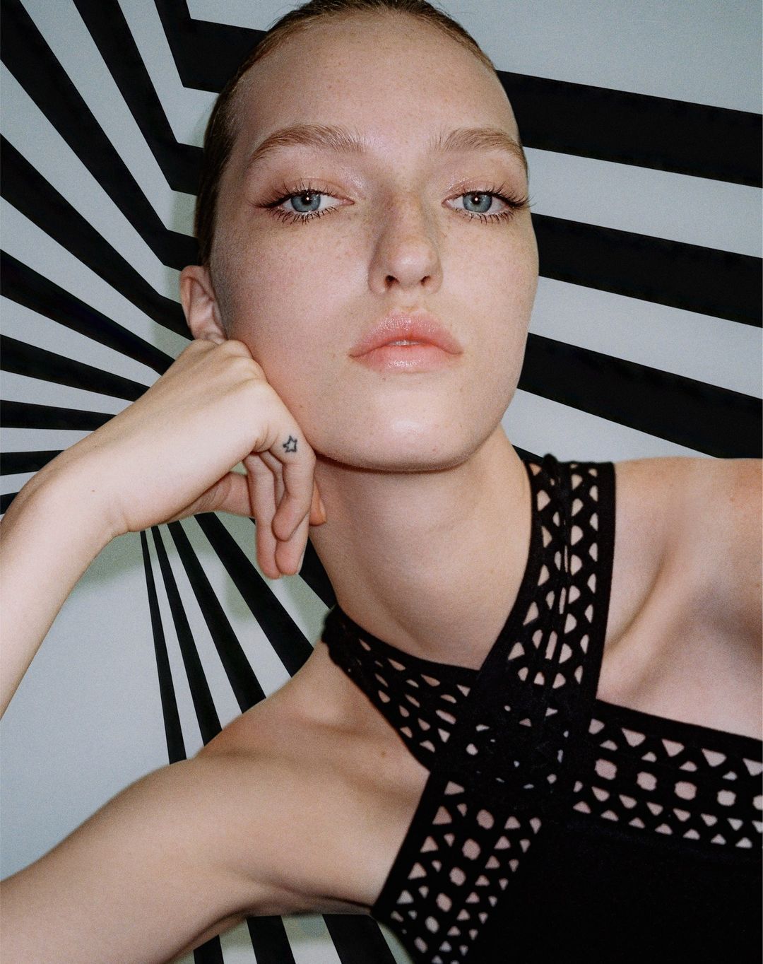 Close-up portrait of a woman in a black halter top posing against a dynamic black and white striped background.