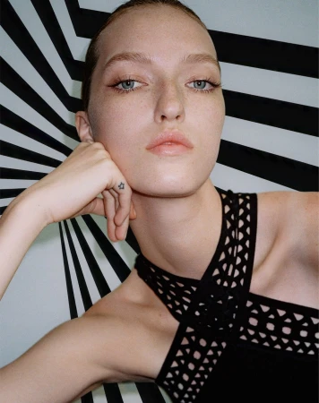 Close-up portrait of a woman in a black halter top posing against a dynamic black and white striped background.