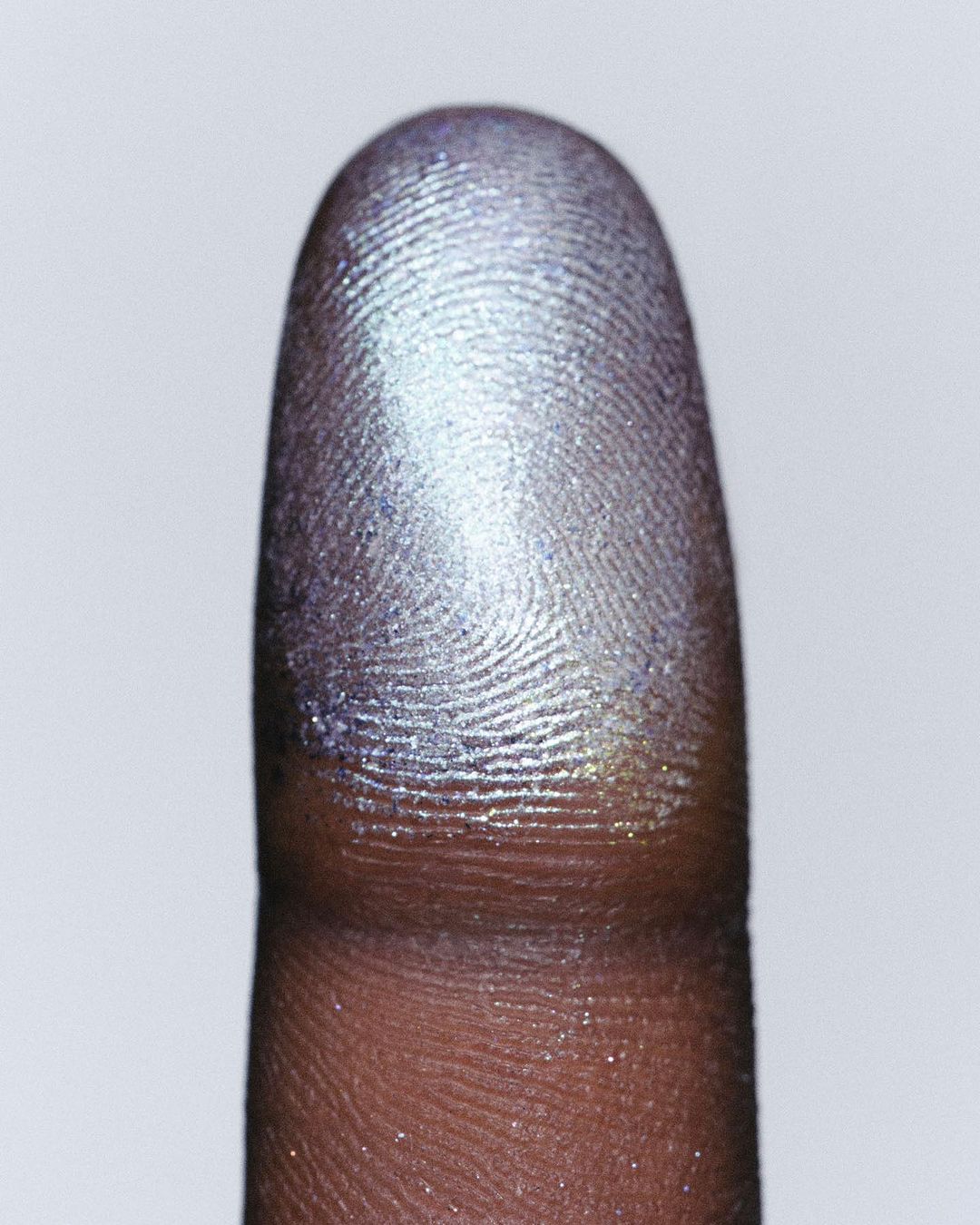 Close-up of a finger covered in silver and gold glitter powder, highlighting skin texture and unique fingerprint details.