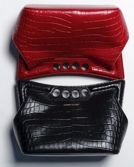 Elevated view of a red and black Alexander McQueen handbag featuring a crocodile skin pattern and circular cut-out handle detail.