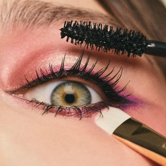 Close-up of an adult female eye being styled with an eyeliner brush and mascara wand, highlighting makeup application.