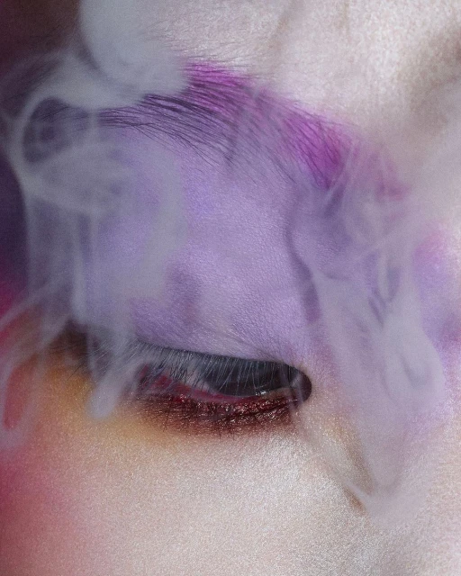 Close-up studio shot of an adult female face with closed eyes, purple makeup, and vapor-like smoke around her face.