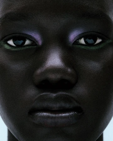 Close-up portrait of a dark-skinned person with colorful makeup on their eyes, set against a pale background in a beauty shot.