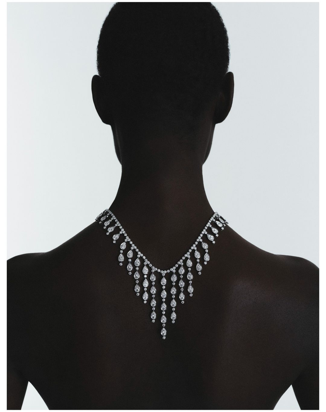Elegant high jewelry diamond necklace showcased on a model's silhouette against a bright white background in a minimalist studio setting.