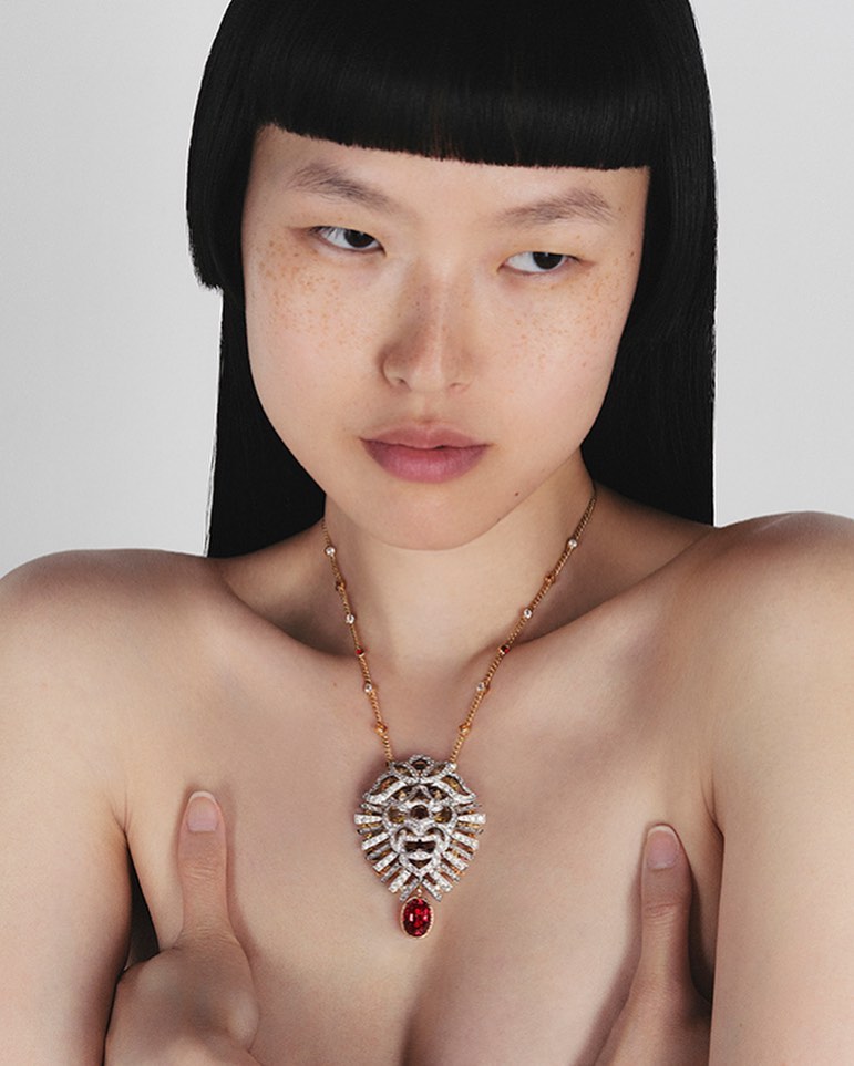 Asian woman with blunt black bob, wearing a lion-shaped pendant necklace with rubies against a bright white studio backdrop.
