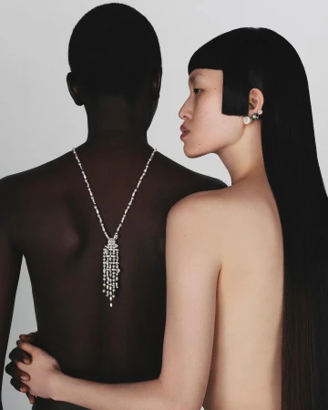 Two models posed closely together against a neutral background wearing a diamond necklace and earrings.
