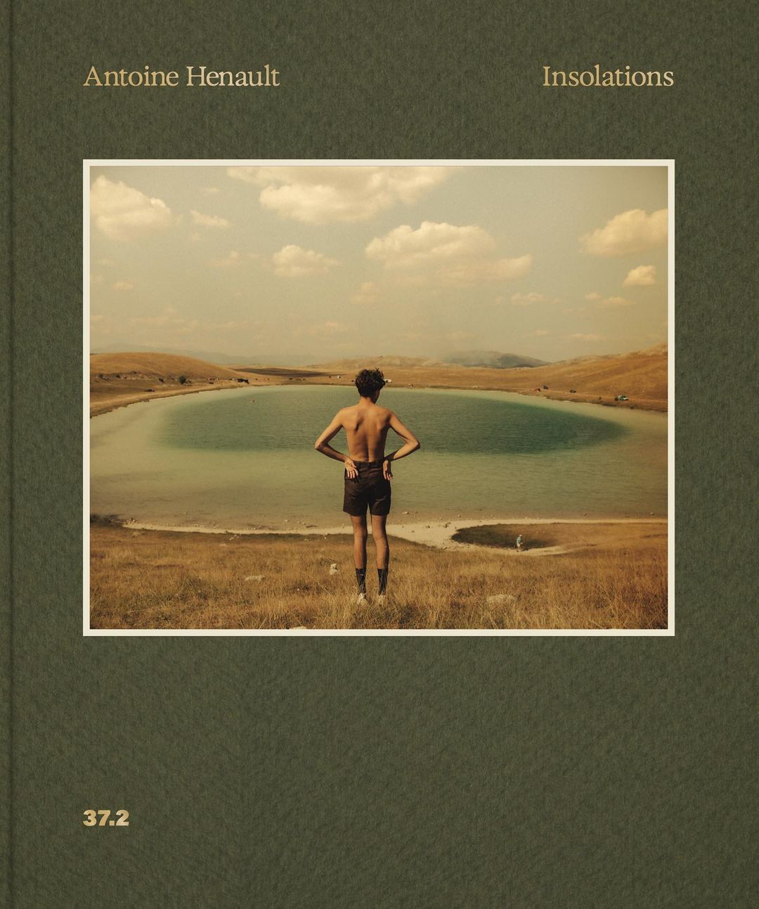 Person stands at the edge of a grassy hill looking at a lake surrounded by a field under a cloudy sky in a book cover image.