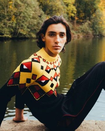 Young man with dark hair wearing a patterned yellow knit sweater by a lake, photographed by Antoine Henault