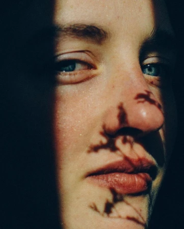 Close-up portrait of a person with blue eyes and intricate foliage shadow patterns cast across their face by Antoine Henault.