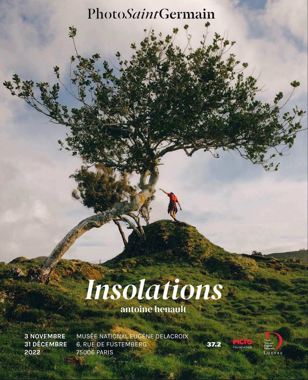 Outdoor poster featuring a lone figure atop a grassy hill, set beneath a sprawling tree against a cloudy sky, advertising a Photo Saint Germain exhibition.