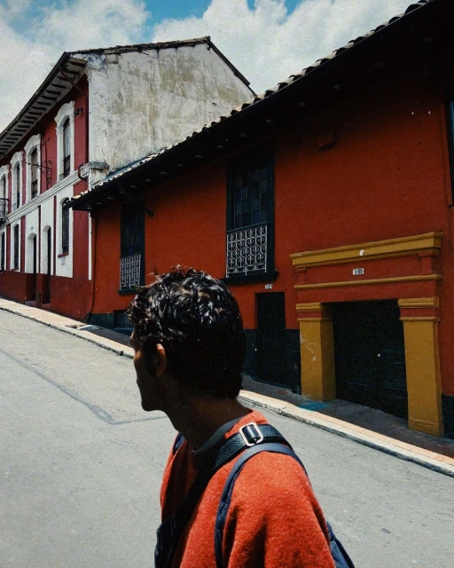 Adult male in a red sweater walks on a city street alongside colorful buildings under a bright sky, captured with natural light.