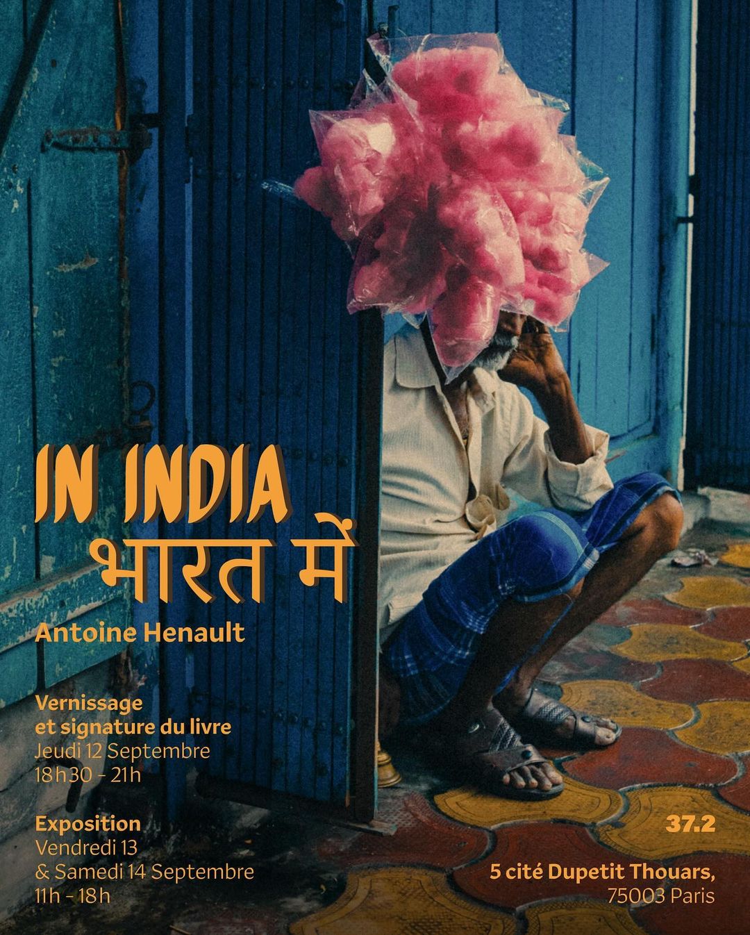 Poster featuring an elderly Indian man squatting next to a blue door, holding a large collection of pink cotton candy bags on his head.