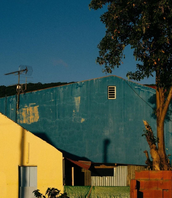 A blue house with an antenna on the roof next to a yellow house with a tree in front of it under a clear blue sky.