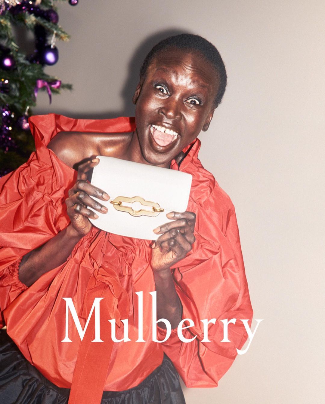 Fashion shot featuring a smiling Black woman with a Mulberry purse in front of a decorated Christmas tree, wearing a red ruffle top.