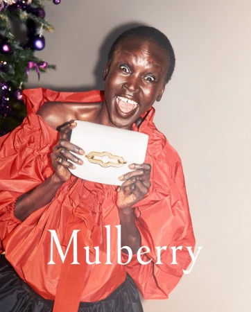 Fashion shot featuring a smiling Black woman with a Mulberry purse in front of a decorated Christmas tree, wearing a red ruffle top.