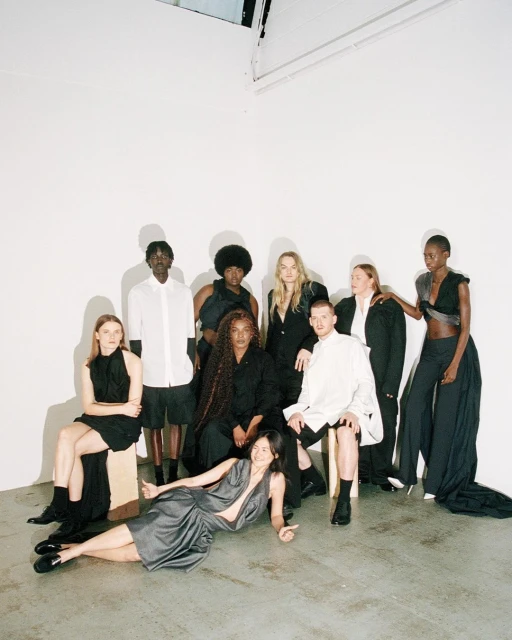 Group of nine diverse fashion models posing indoors in black, white, and gray clothing against a white background, showcasing modern style.