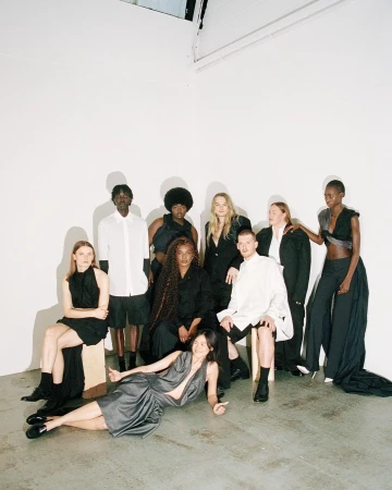 Group of nine diverse fashion models posing indoors in black, white, and gray clothing against a white background, showcasing modern style.