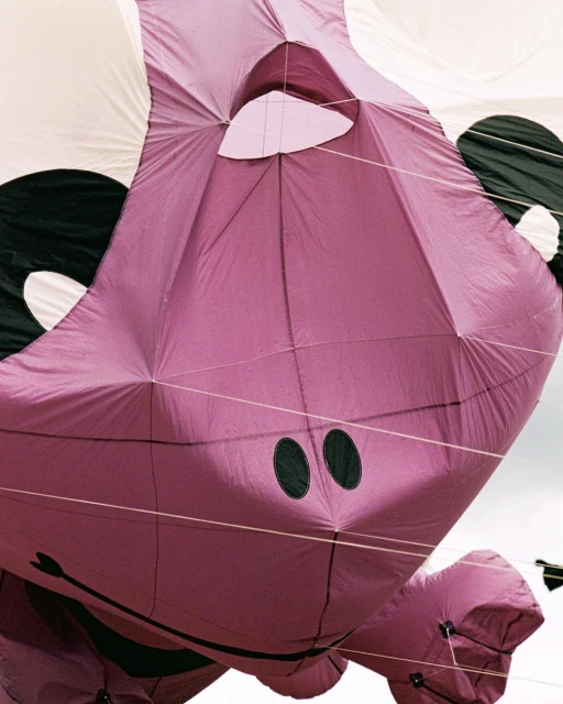 Close-up of a large, inflated purple hippo kite with black accents against a cloudy white sky, showcasing its unique design.