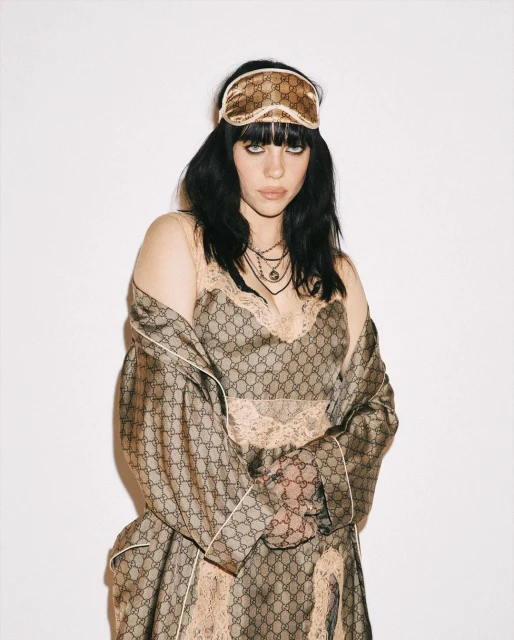 Portrait of a woman wearing a Gucci robe and sleep mask with a neutral expression against a white backdrop in a studio setting.