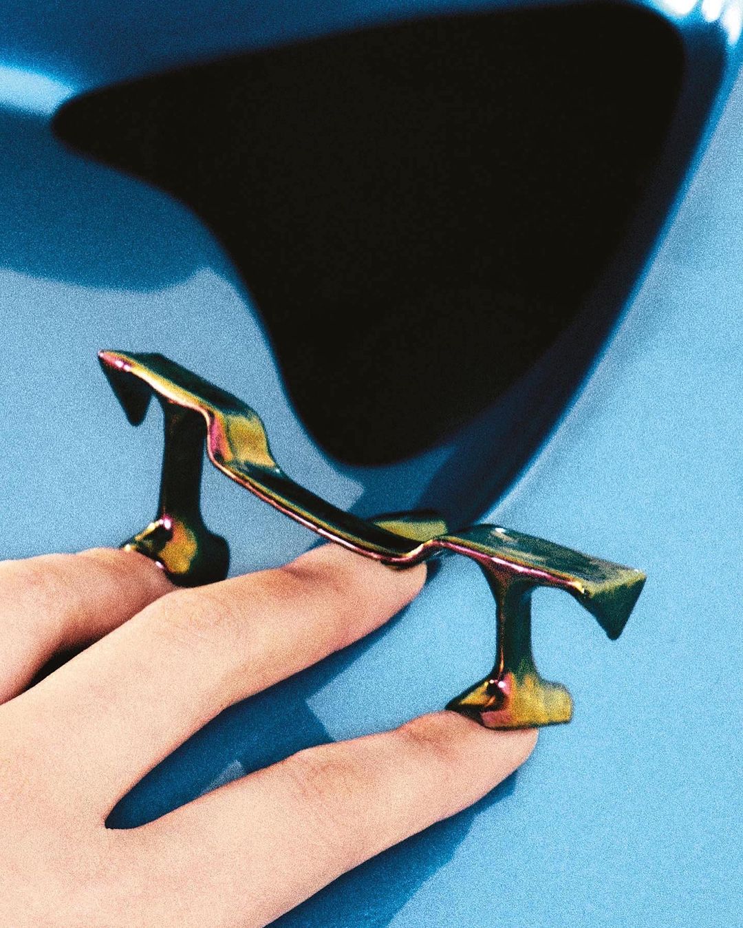 A woman's hand displaying fingernail accessories that resemble a car spoiler on a light blue background in an indoor setting.
