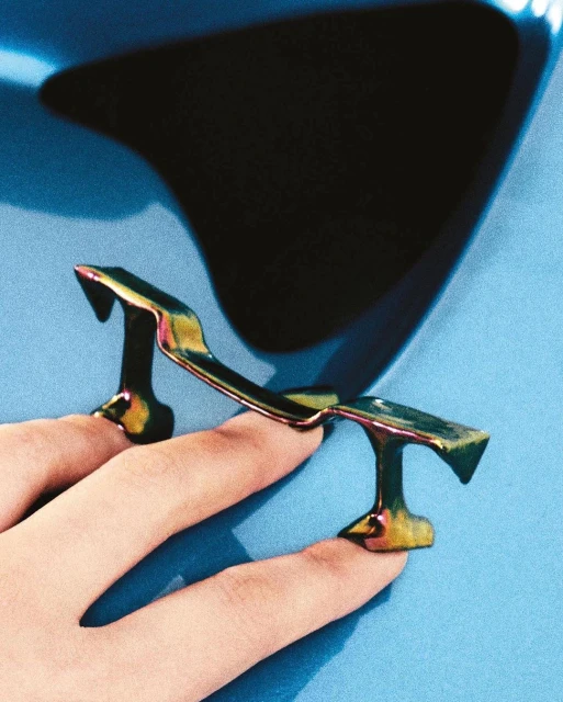 A woman's hand displaying fingernail accessories that resemble a car spoiler on a light blue background in an indoor setting.