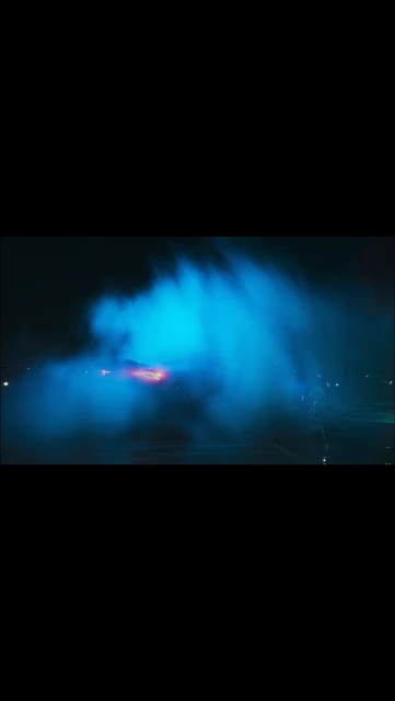 Vibrant blue light and smoke rise in a dark outdoor setting, creating an abstract and dynamic visual display at nighttime.