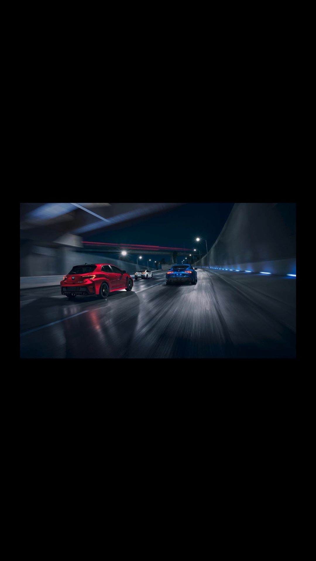 Three cars, red and blue, speed through a dark tunnel with glowing lights. Motion blur enhances the sense of speed.