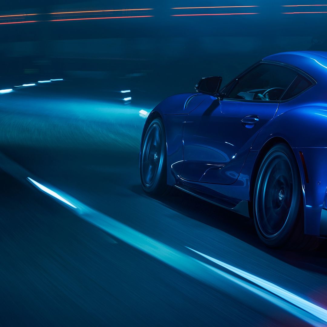 A blue sportscar drives on a dark road at night with lights blurred from long exposure creating an intense sense of speed.