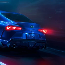 Rear view of a blue sports car driving at night with glowing red taillights and dual exhaust pipes on a dark highway