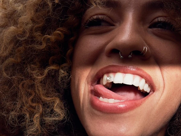 Close-up portrait of a woman with curly hair, septum piercing, and a star tooth gem, sticking her tongue out.