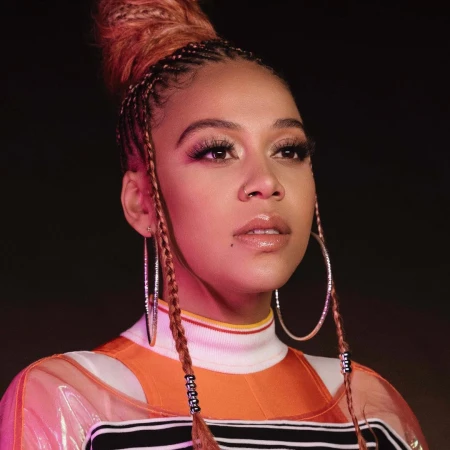 Portrait of a woman with braided hair and hoop earrings wearing an orange top, photographed by Antonia Steyn.