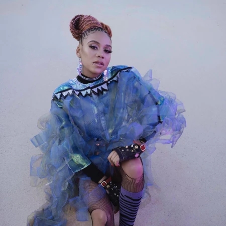 Portrait of a woman with braided hair wearing a blue tulle dress with decorative elements and fishnet stockings in a studio setting.