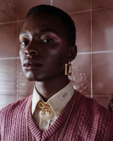 Portrait of a Black man wearing a pink knitted vest and gold earrings against pink tiles by Antonia Steyn