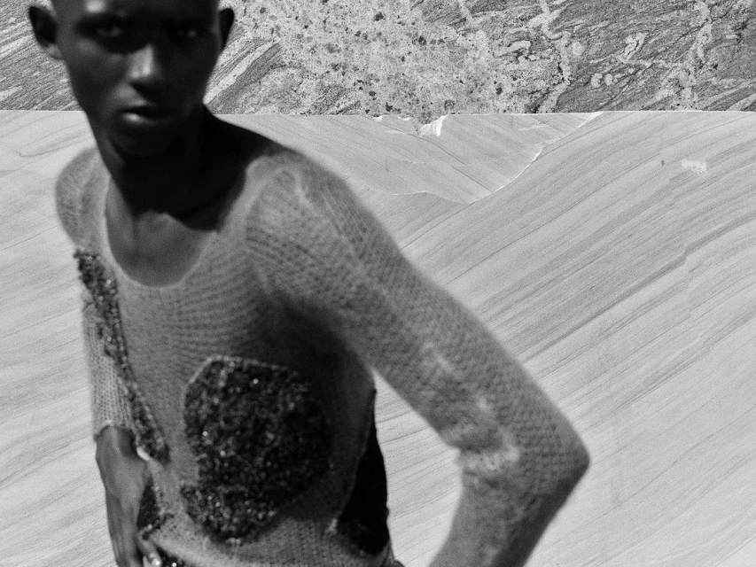 Monochrome portrait of a young Black man in a textured sweater with embellishments, set against a split abstract landscape background.