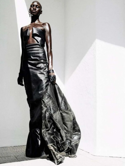 A dark-skinned model poses in a dark, high-fashion, avant-garde dress with strong studio lighting, creating a striking and dramatic image.