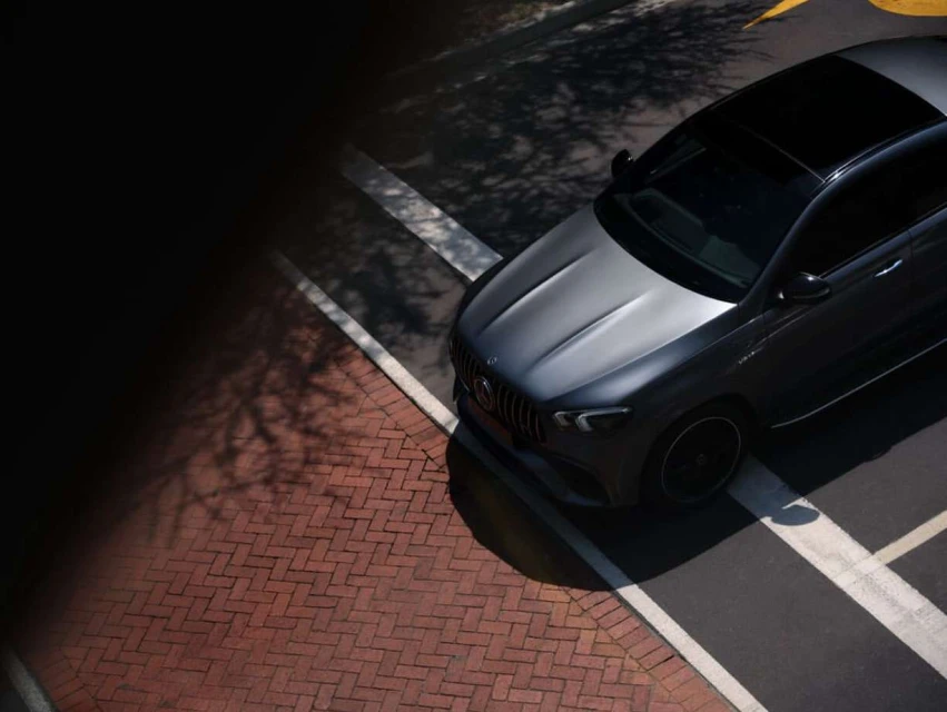 Aerial view of a dark grey Mercedes-AMG GT 63 S parked on a brick paved area with harsh shadows, showcasing automotive design.