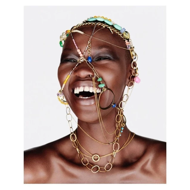 Close-up of a smiling African woman adorned with colorful beaded jewelry around her head and neck against a plain white background.