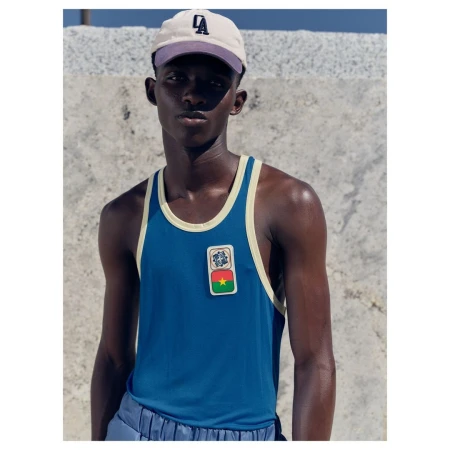 Black man wearing a blue tank top and a baseball cap against a stone wall background photographed by Antonia Steyn
