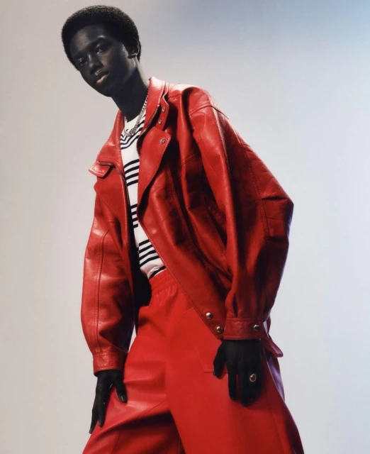 Fashion shot of a single Black male model wearing a red leather jacket and matching pants, posing against a gradient background.