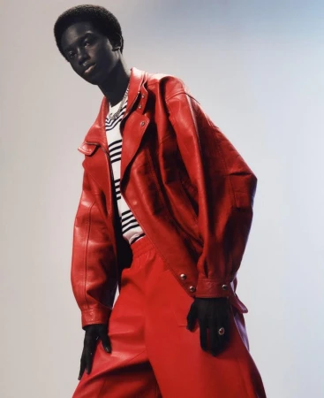 Fashion shot of a single Black male model wearing a red leather jacket and matching pants, posing against a gradient background.