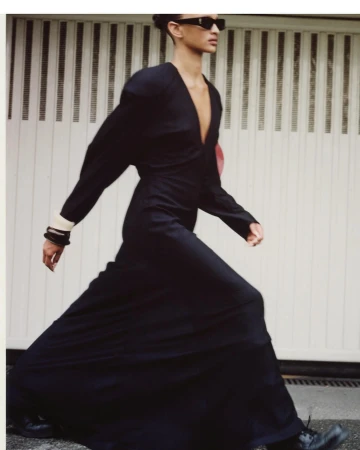 Model in a long black dress and sunglasses walking in front of a white garage door by Antonio Dicorato