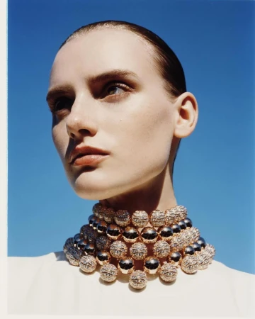 Close up portrait of a woman wearing a heavy gold beaded choker necklace against a clear blue sky