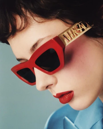 Close-up portrait of a woman wearing chunky red sunglasses with gold temples and a bright blue blazer.
