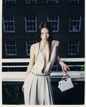 Model in pale plunging dress holding a small white handbag on a rooftop balcony photographed by Antonio Dicorato
