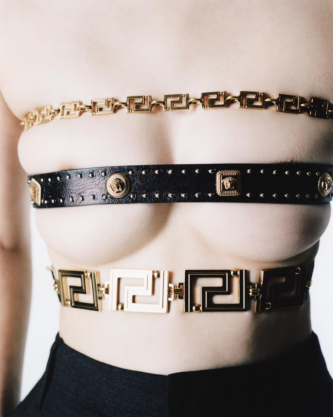 Woman wearing three gold Versace belts around torso against white background. Fashion shot showcasing brand's design and style.