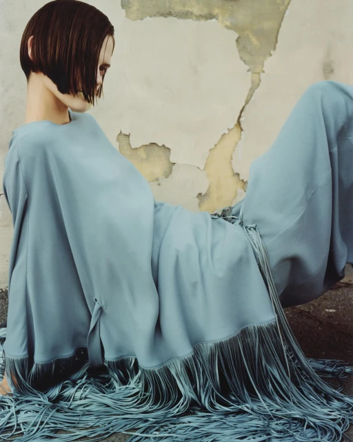 A fashion shot shows a person in a light blue fringe dress lying down against a grungy wall, embodying editorial style and unique textures.