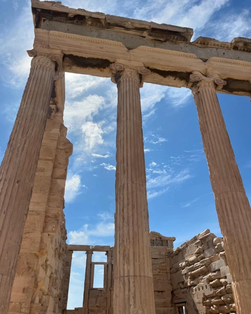 Low-angle shot of the Erechtheion, Athens, featuring ancient stone columns under a blue sky with sparse clouds on a sunny day.