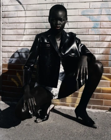 Model wearing a black leather jacket crouching against a brick wall in Paris captured by Antonio Dicorato